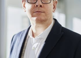 Profile portrait of a confident business executive wearing eyeglasses in a sunlit office setting.